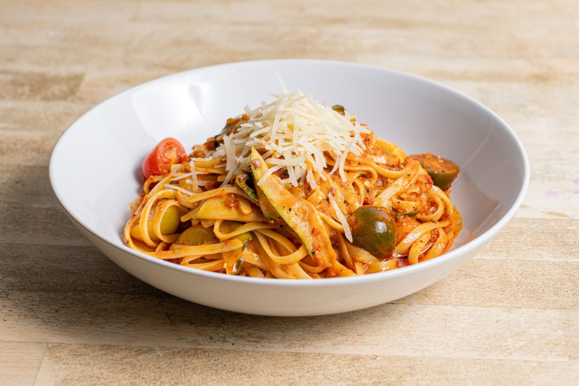 A white bowl filled with spaghetti and vegetables on a wooden table.