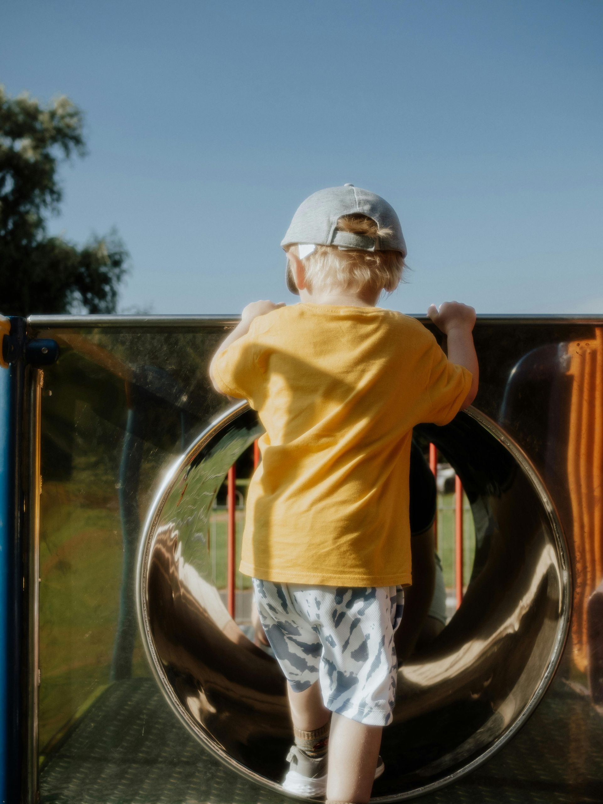 A young boy in a yellow shirt is playing in a playground.