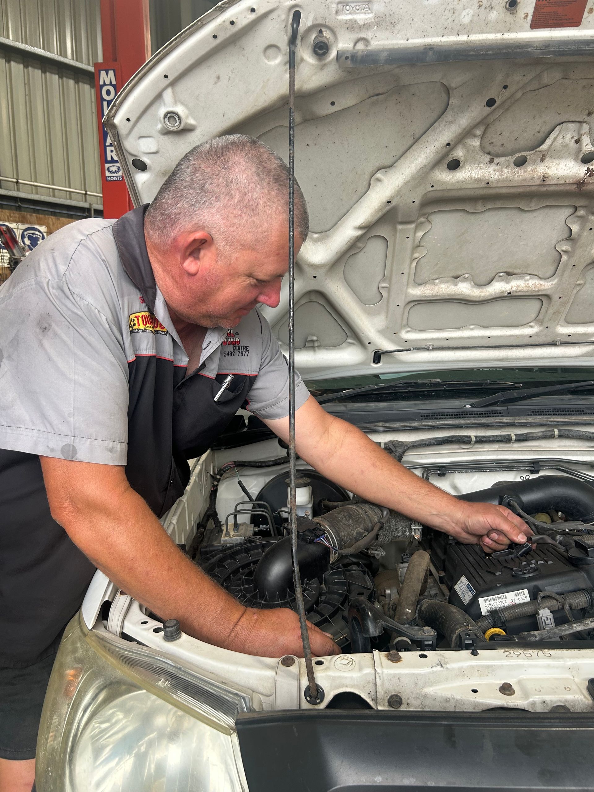 Mechanic inspecting an engine under the open hood of a white car in a garage.  — Gympie Diesel & Dyno Centre in Glanmire, QLD