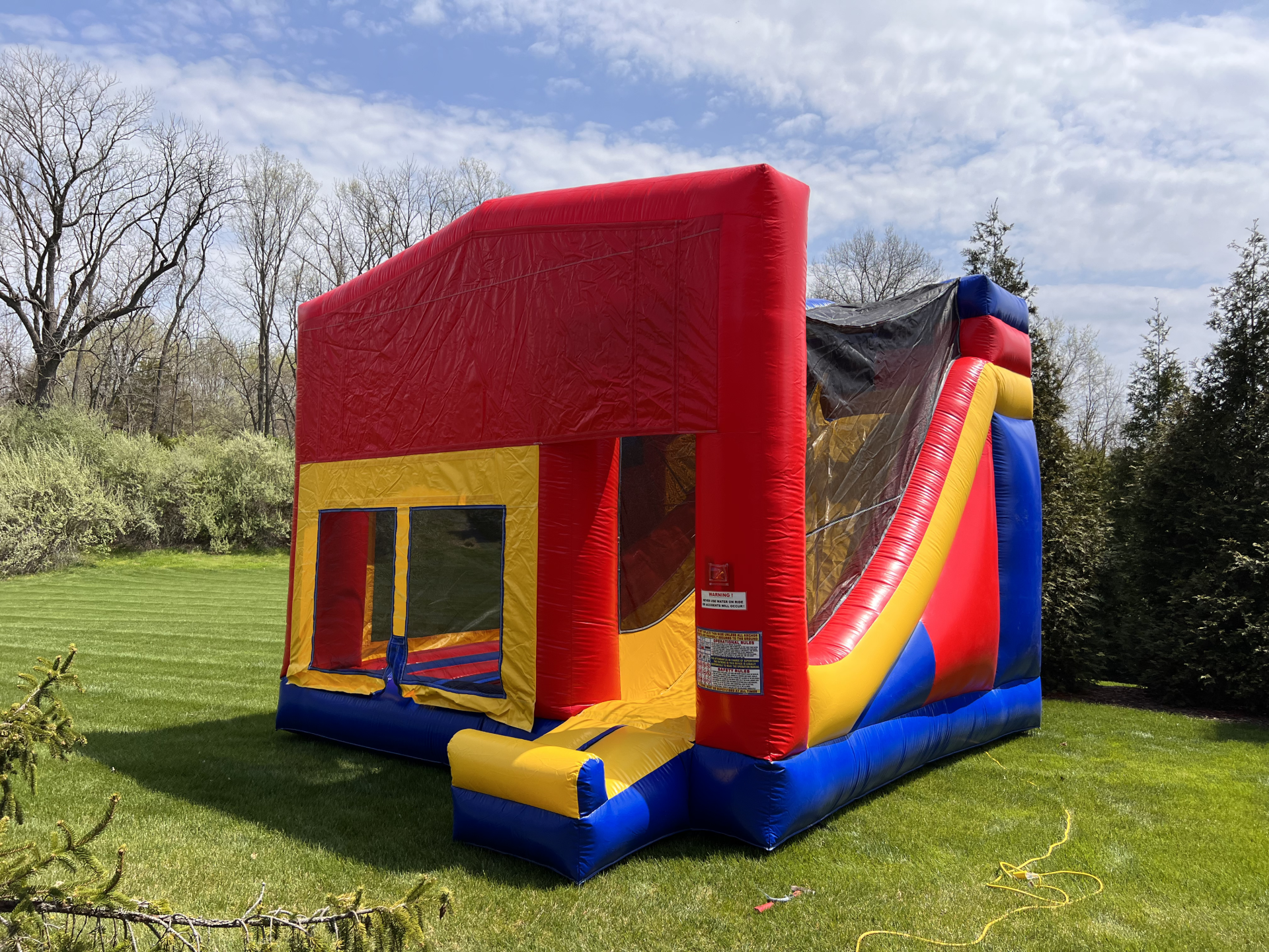 A red , yellow , and blue bouncy house with a slide is sitting on top of a lush green field.