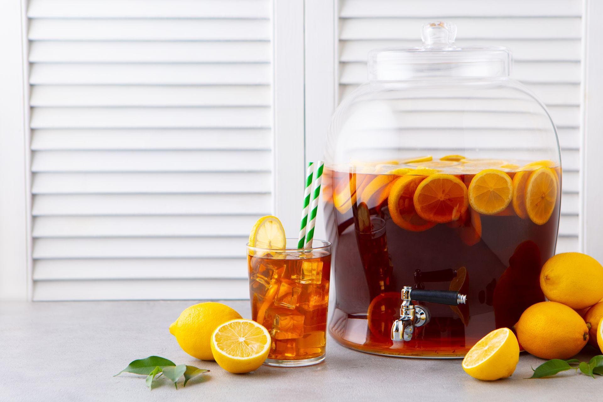 A pitcher of iced tea with lemons and a glass of iced tea on a table.