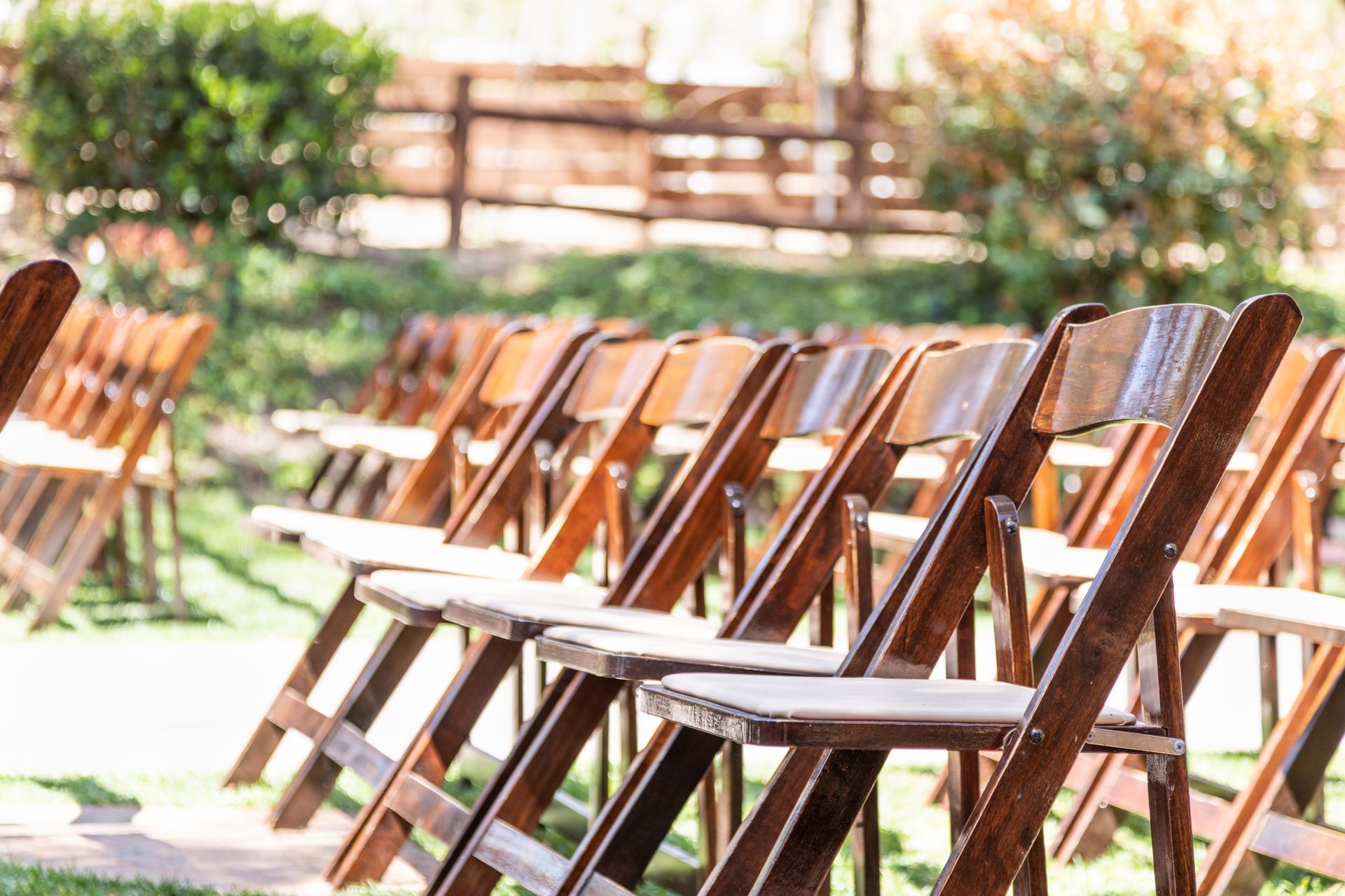A row of wooden folding chairs sitting on top of a lush green field.