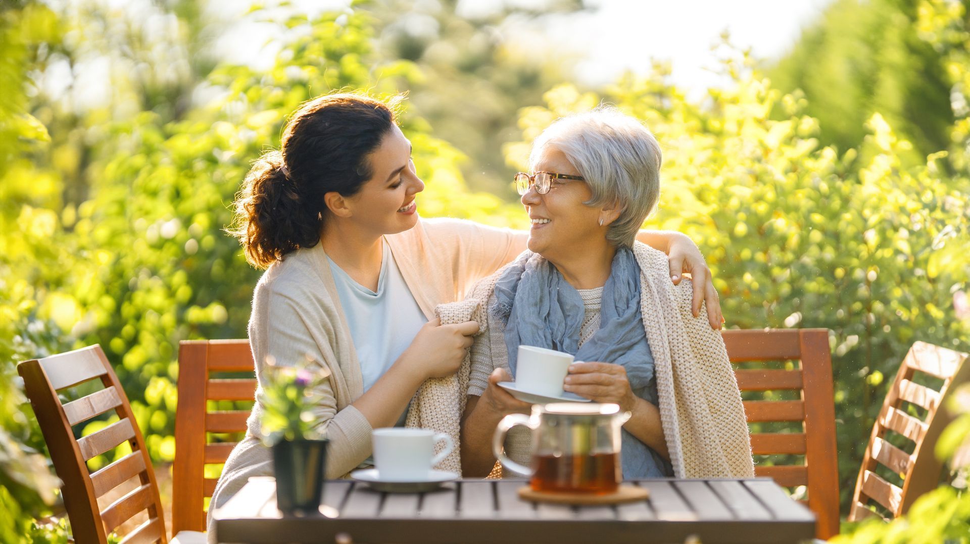 Woman wraps an elderly person in a blanket outdoors, smiling.