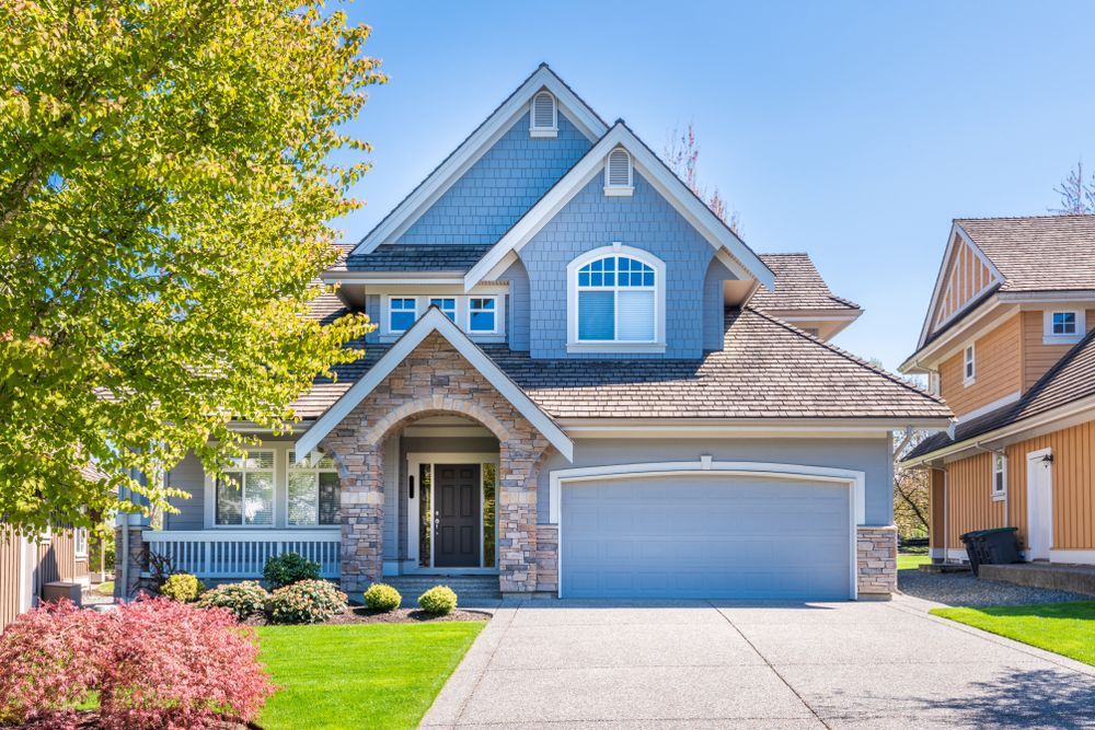 Blue suburban house with stone accents, front porch, and two-car garage on a sunny day
