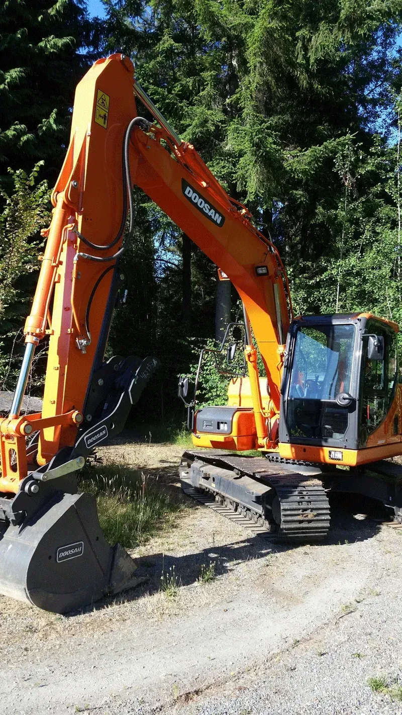 Orange Doosan excavator on gravel with a forest background.