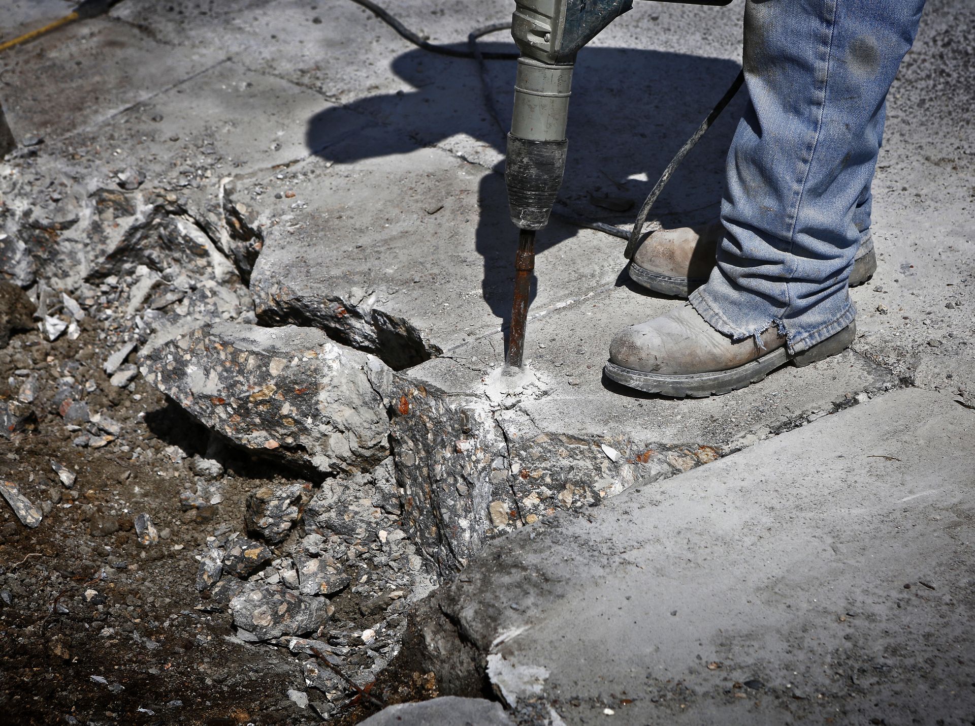 A person using a jackhammer to break up concrete, outside in daylight.