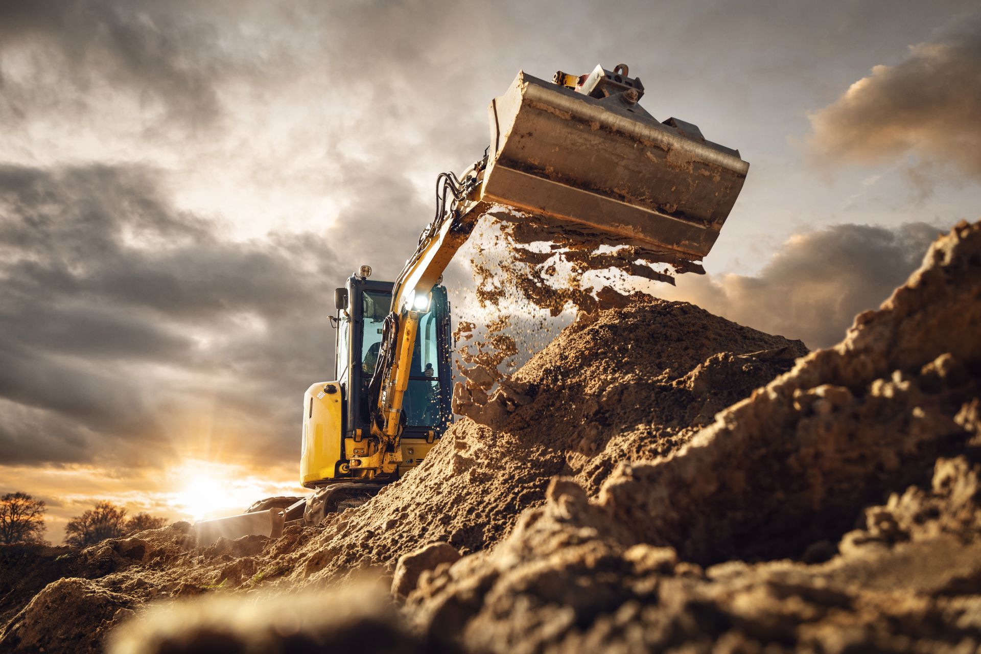 Excavator scoops dirt in a construction site at sunset.