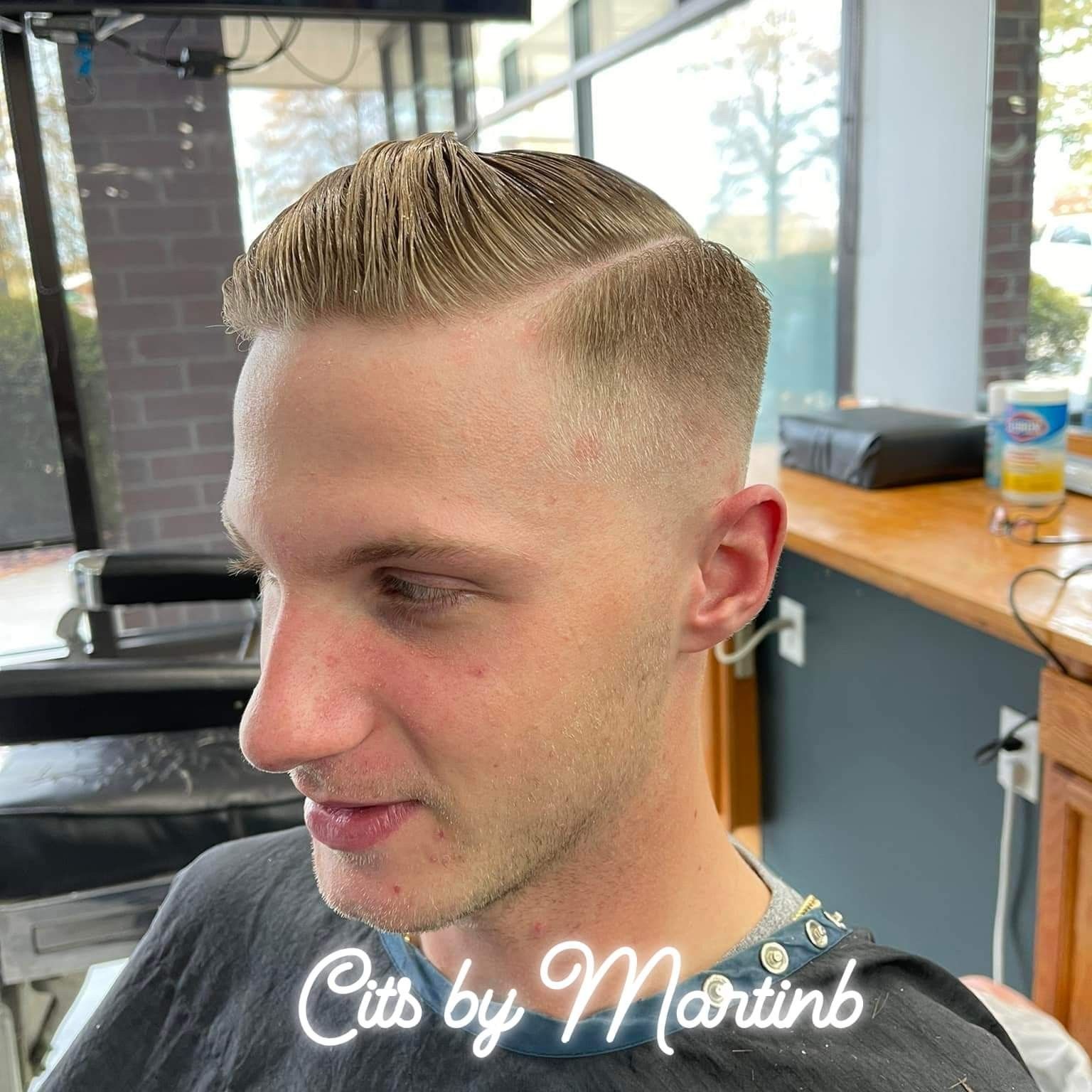 A barber chair view of a man with a short, tapered haircut featuring a clean side part, styled in a salon.