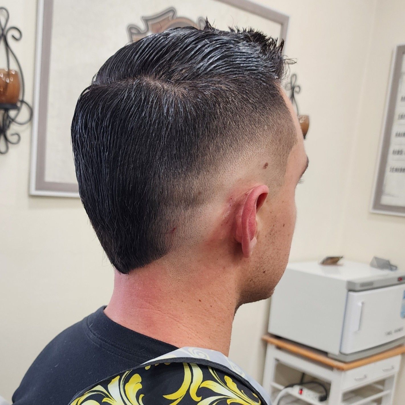 A person with a dark, short-sided fade haircut styled into a textured mohawk, viewed from the side in a salon setting.