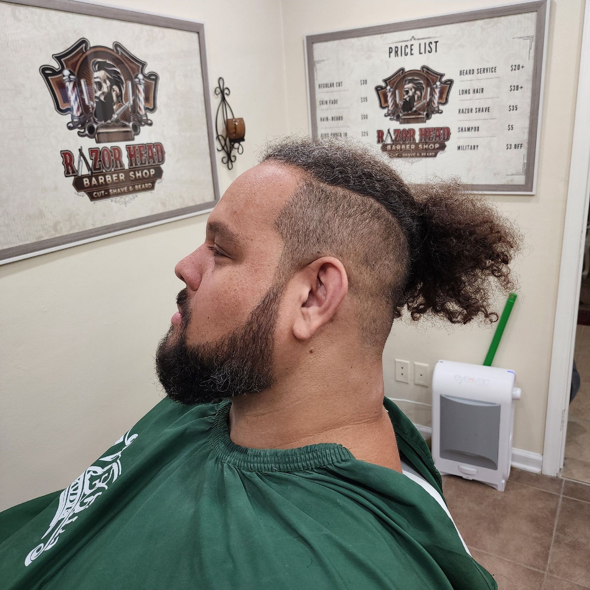 Side view of a person with a shaved undercut and ponytail, wearing a green cape in a barbershop.