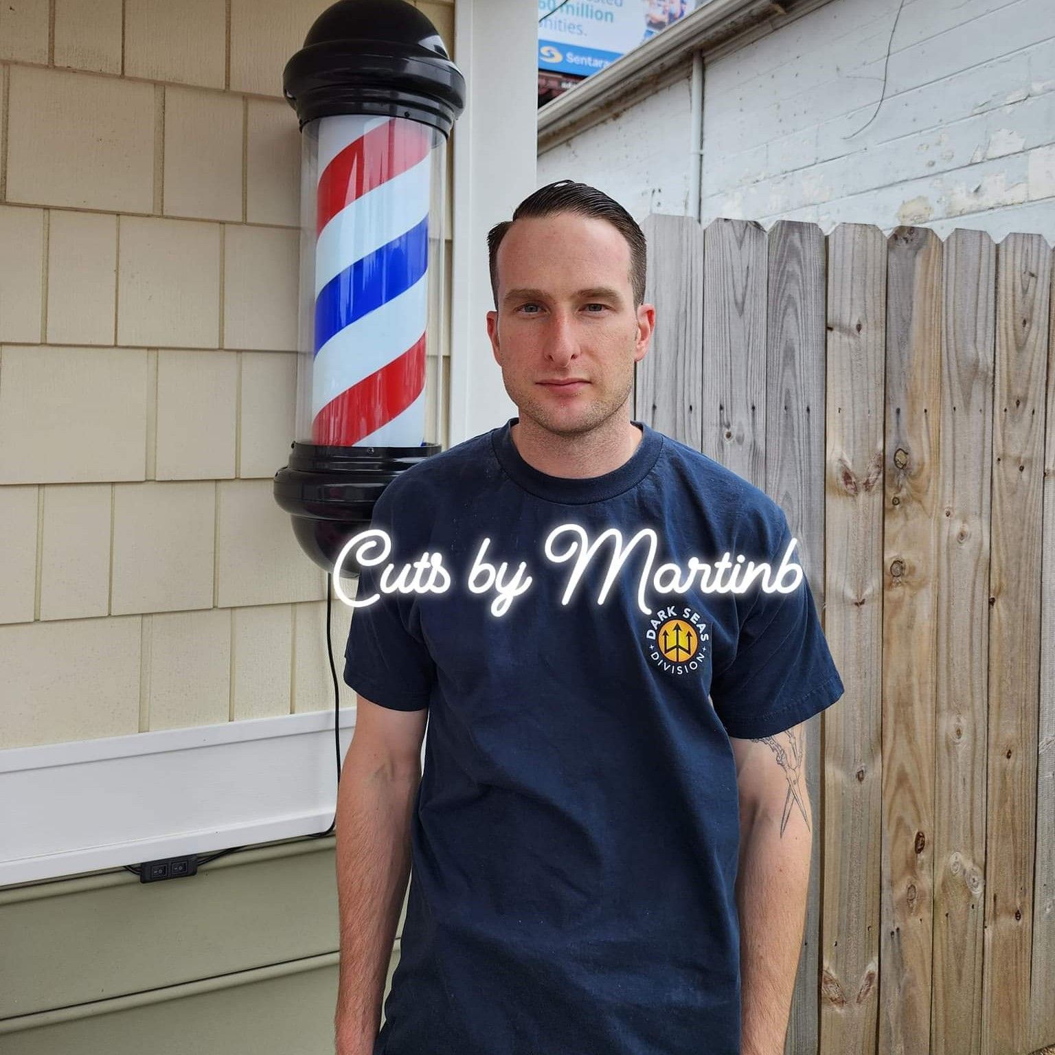 A person wearing a dark blue t-shirt stands in front of a barber pole with the text 