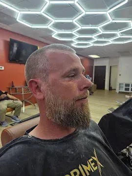 Man with a beard in a dim room under hexagonal ceiling lights, seated in profile and looking right
