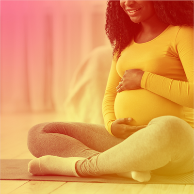 Pregnant person sitting cross-legged on a yoga mat, gently holding their belly and smiling.