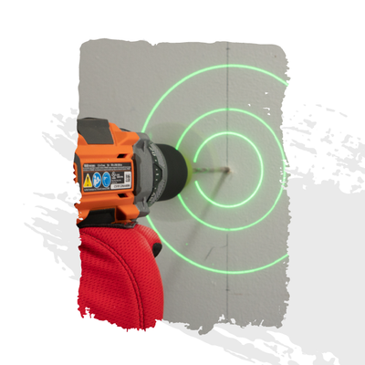 Orange drill with red glove drilling into a gray wall, with green concentric laser target circles.