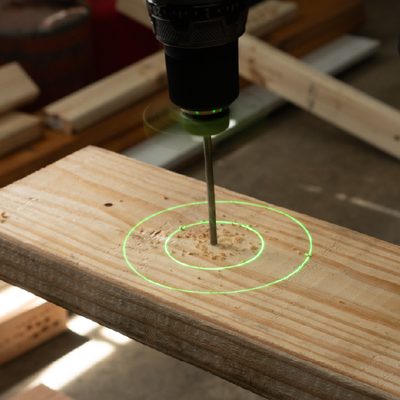 Drill press boring a hole into a wooden plank with green alignment rings visible