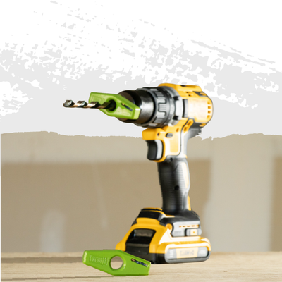 Yellow-and-black cordless drill with a green drill bit on a work surface