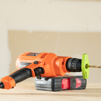 Orange cordless drill on a battery pack with a green bit, resting on a wooden surface