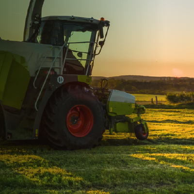 Green tractor in a field at sunset, with orange wheels and a low horizon.