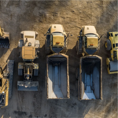 Top-down view of yellow dump trucks and excavators in a dirt construction site.