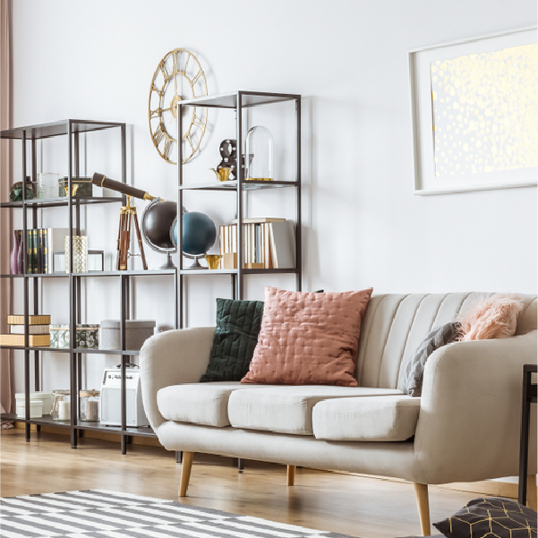 Bright living room with a beige sofa, colorful pillows, and open shelving with decor and books.