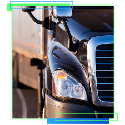 Close-up of a black semi-truck cab with chrome grille and headlight on a highway