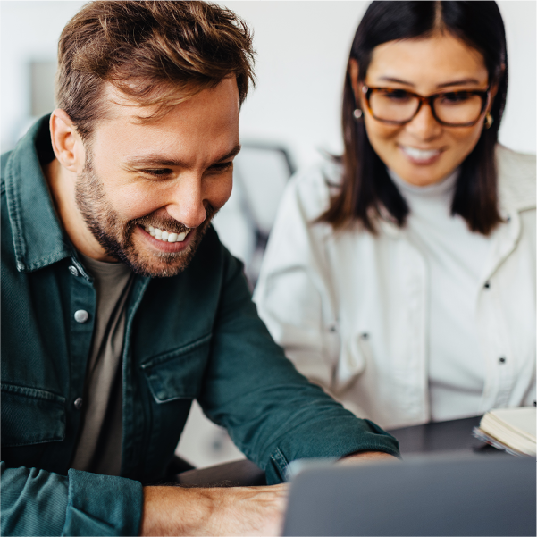 Two coworkers smiling and looking at a laptop in an office setting