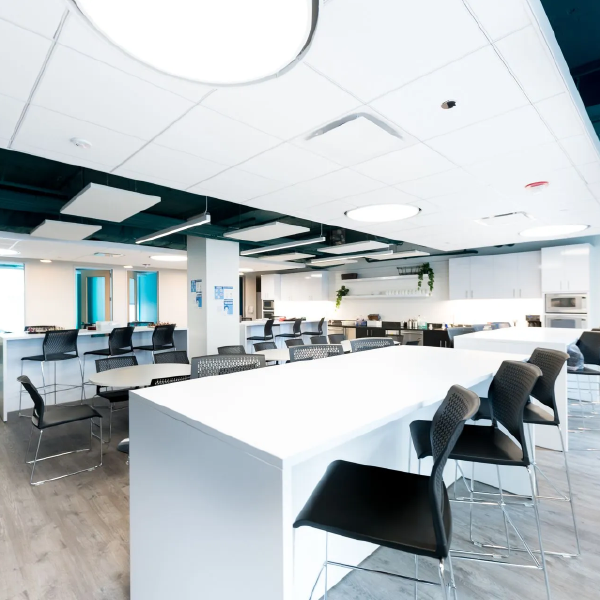 Bright modern office with white tables, black chairs, and large windows, mostly empty