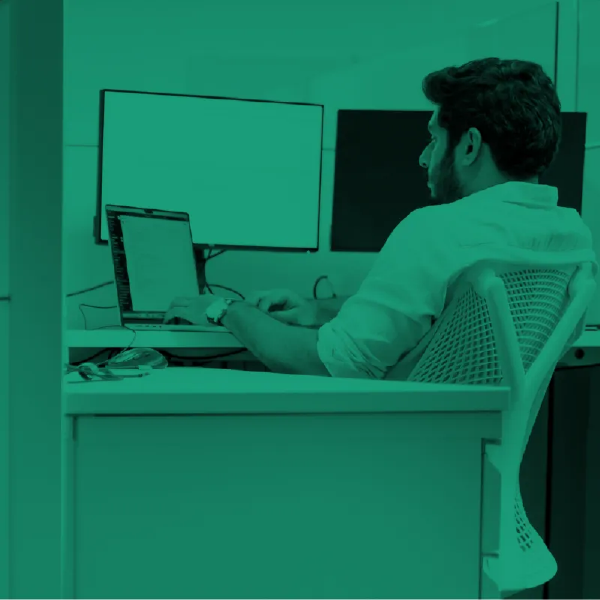 Person working at a desk with a laptop and dual monitors in a green-tinted office