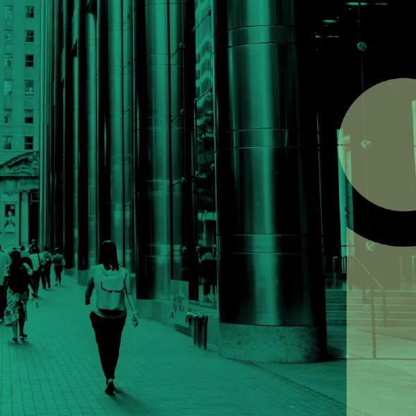 People walking on a city sidewalk beside tall glass buildings, tinted green.