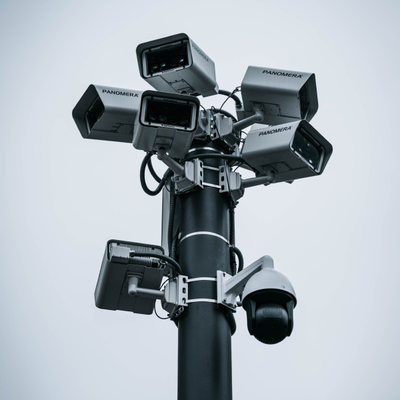 Multiple security cameras mounted on a tall pole against a gray sky