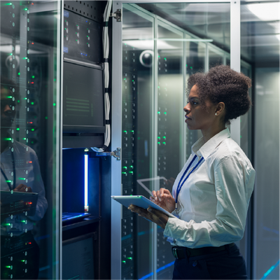 Technician holding a tablet in a glass-walled server room, inspecting illuminated rack equipment