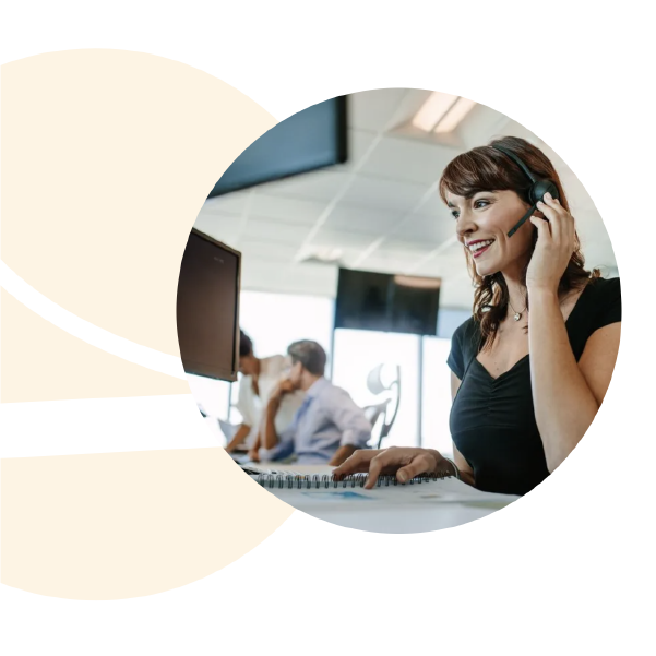 Woman on the phone at a computer in an office with coworkers in the background