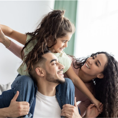 Smiling family embracing on a couch, with a child leaning over two adults in a bright room
