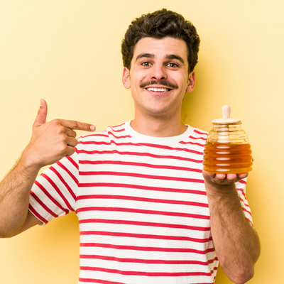 Man in striped shirt holding a honey jar and pointing at it against a yellow background