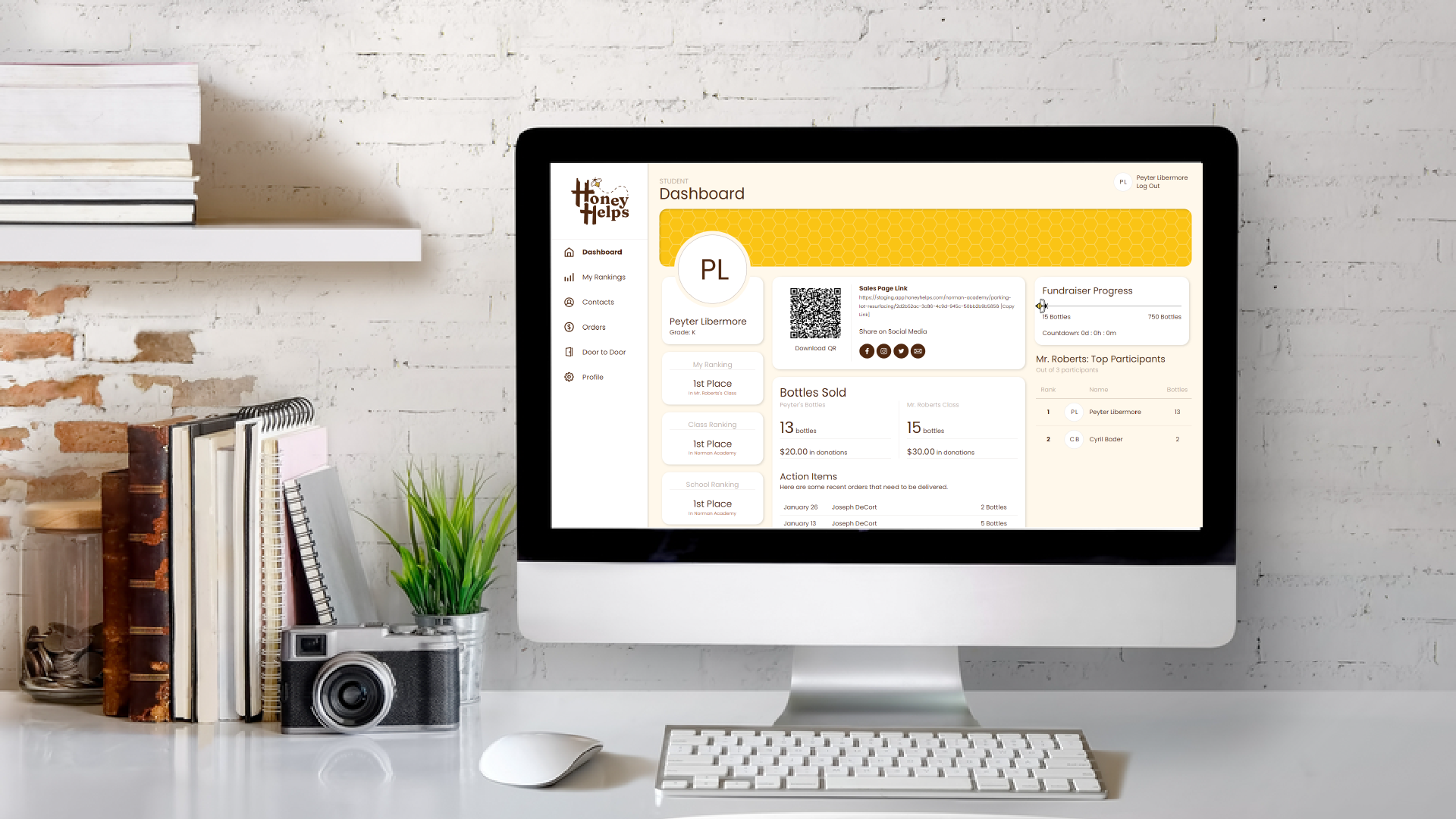 Desktop computer on a white desk displaying a web dashboard, with keyboard, mouse, books, camera, and plant nearby.