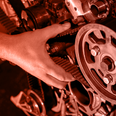 Hand adjusting gears and a wheel inside a red-lit engine or machinery mechanism