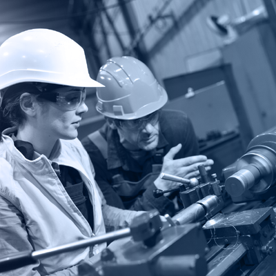 Two workers in hard hats inspecting machinery in a factory workshop