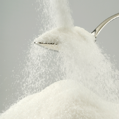 White granulated sugar pouring from a spoon into a pile