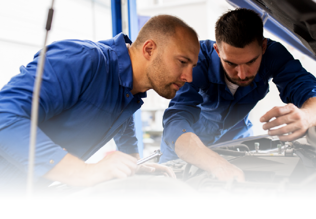 Two technicians in blue shirts inspect machinery together under a tent