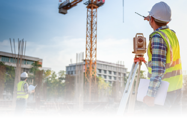 Surveyor in yellow vest using tripod total station at a construction site with cranes and buildings in the background
