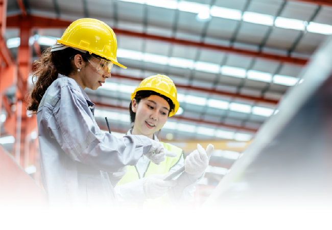 Two engineers in yellow hard hats reviewing plans in a bright industrial facility
