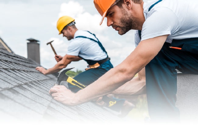 Two roofers in hard hats installing shingles on a sloped roof