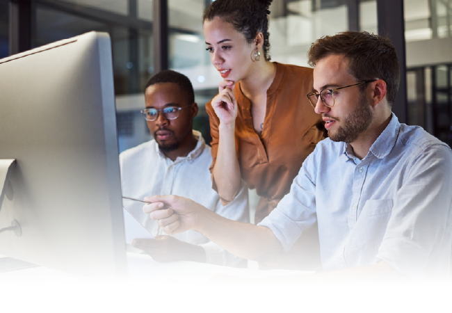 Three coworkers reviewing data on a desktop computer in an office