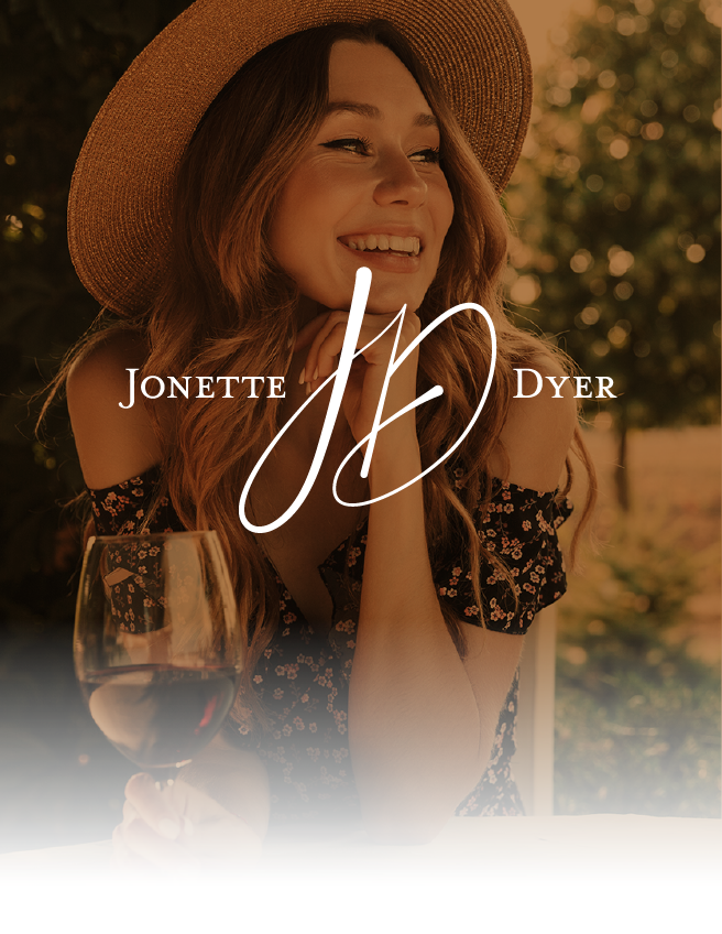 Woman in a straw hat smiling at a table, with white “Jonette Dyer” text overlay.