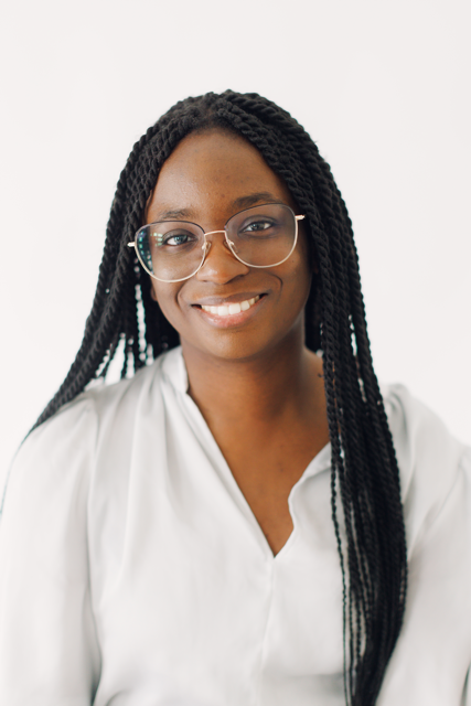 Smiling person with glasses and long braids in a white blouse against a light background