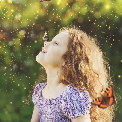 Girl in a purple dress smiling with eyes closed in a sunlit garden, butterflies fluttering around her