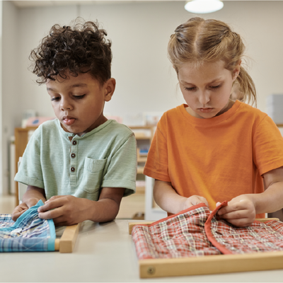 Two children at a table, concentrating on arranging colorful patterned fabric pieces.