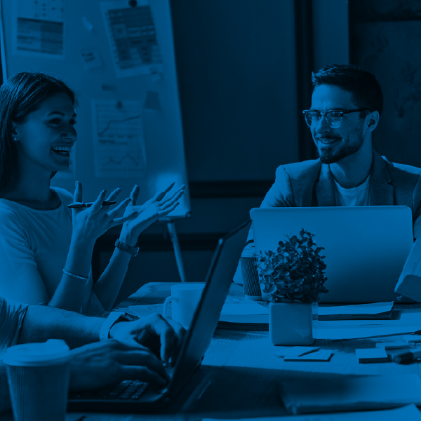 Blue-tinted office meeting with three people talking around laptops and a tablet.