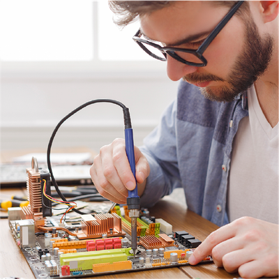 Technician soldering a circuit board at a workbench with tools and electronic components