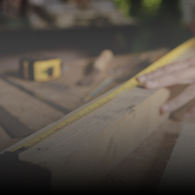 Hand measuring a wooden board with a yellow tape measure on a workbench